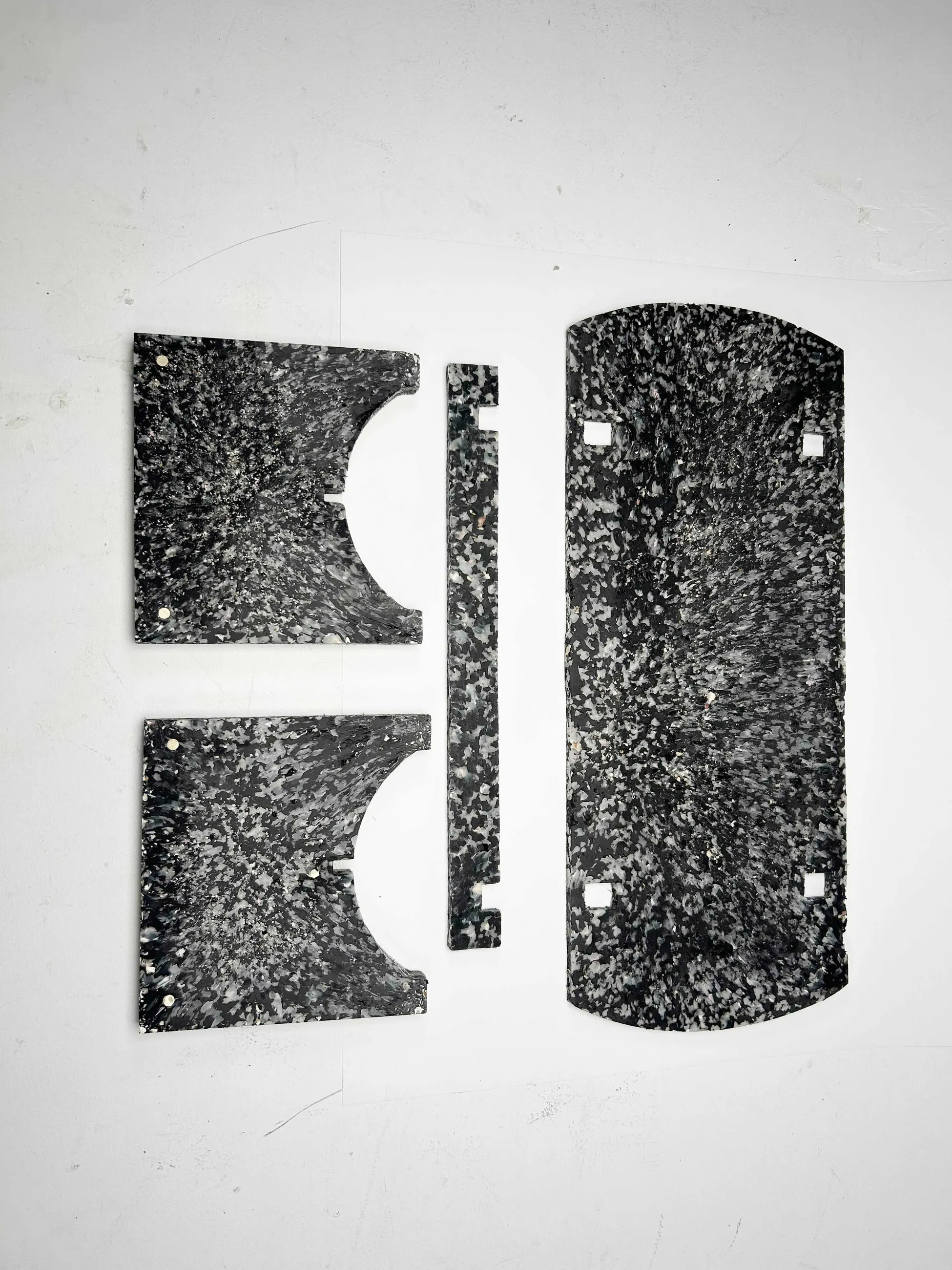 The four flat-pack components of the Shio bench laid out, showing the speckled shell-composite surface.