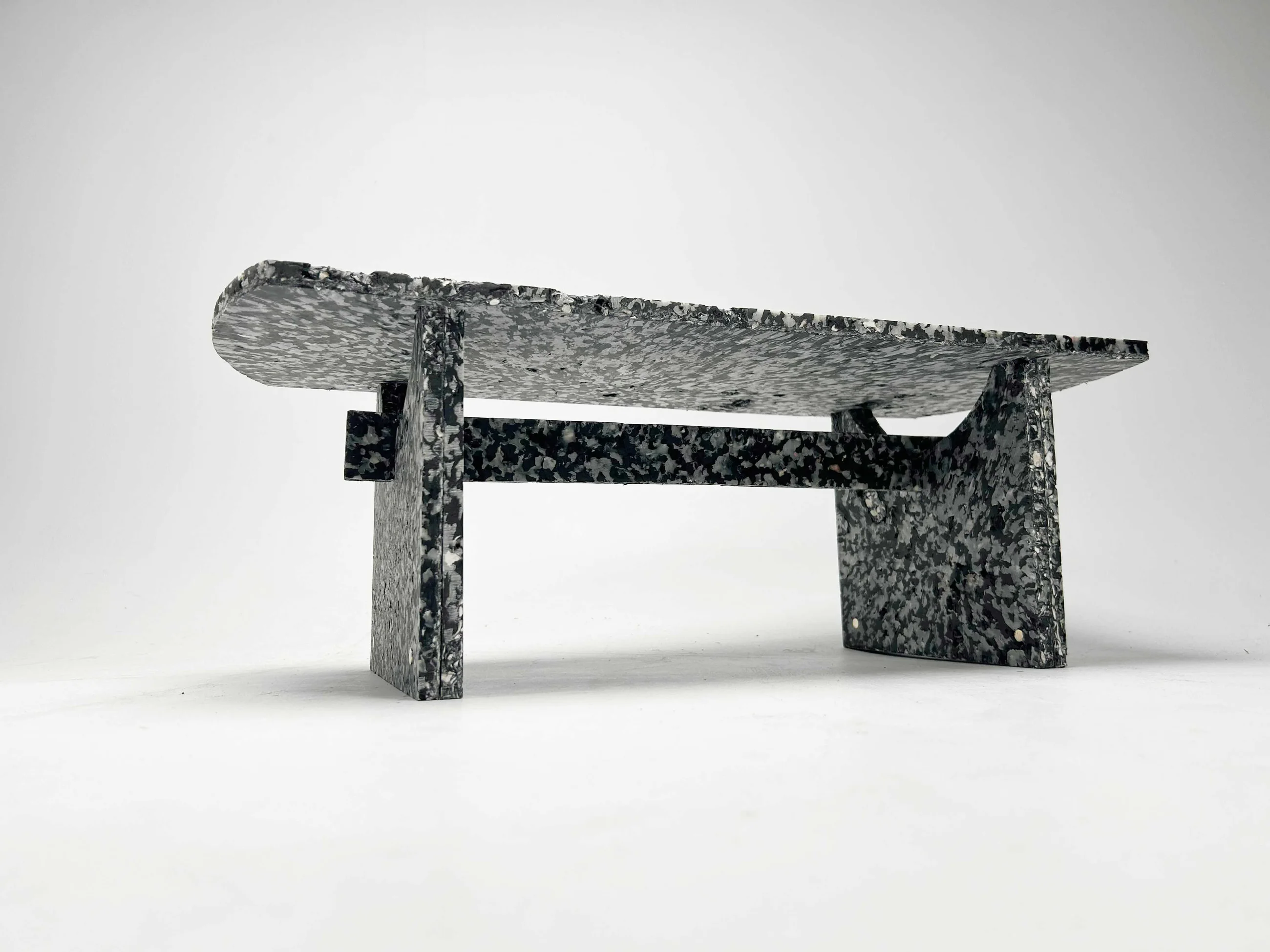 The finished Shio bench in three-quarter view, its speckled composite surface catching the light.
